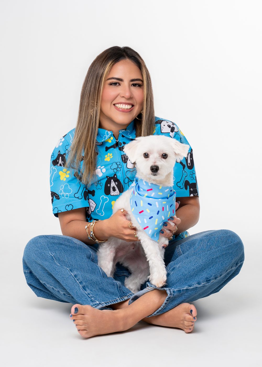 Vanessa Cordova sitting with Bubbles, a small white dog in a sprinkle bandana, after a Fear-Free groom